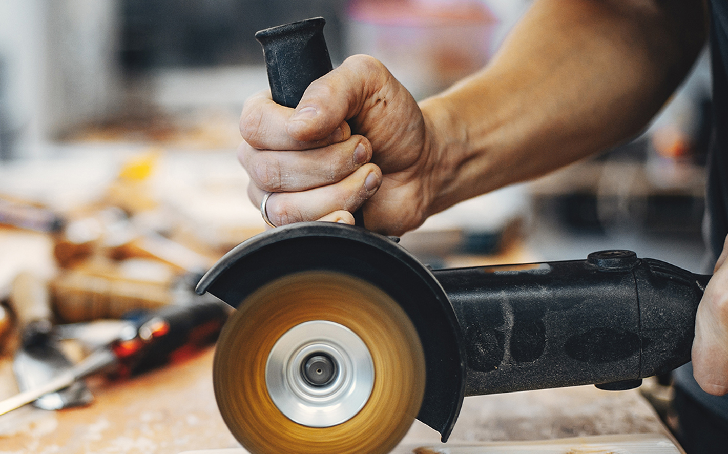 Hand mit Schleifgerät in Werkstatt.