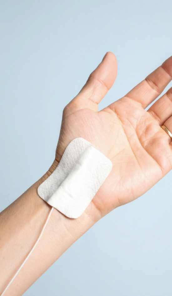 Hand mit Elektrodenpflaster auf hellem Hintergrund.