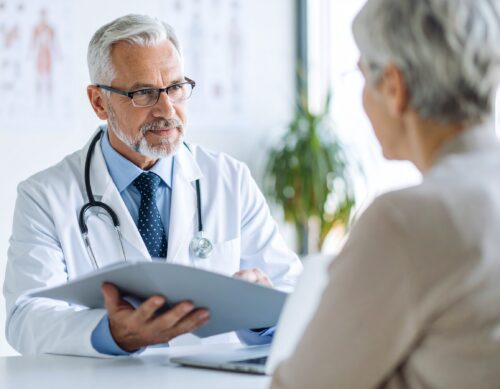 Älterer Arzt spricht mit Patientin im Sprechzimmer.