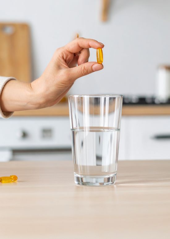 Una mano tiene una capsula sopra un bicchiere d'acqua.